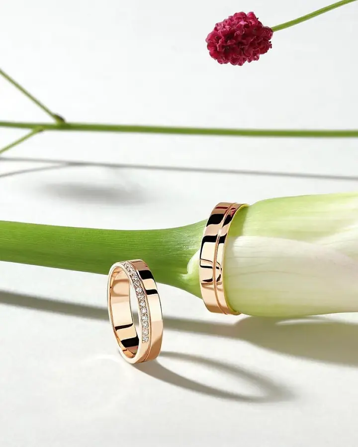 Par de alianças de casamento em ouro rosé sobre flor branca e detalhe em vermelho